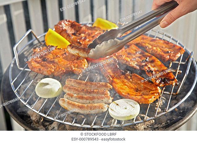 Meat, sausages and vegetables on barbecue, sausage in tongs