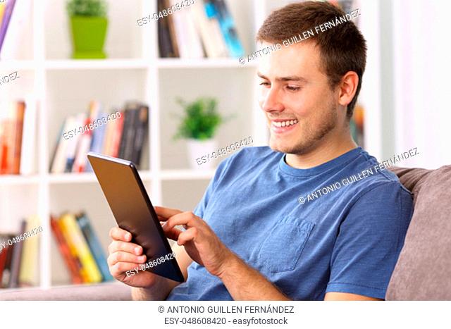 Happy man using a tablet sitting on a sofa at home