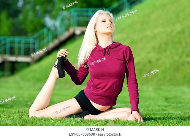 Beautiful young woman doing stretching exercise on green grass at park. Yoga