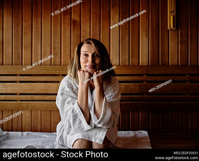 Smiling senior woman with hand on chin sitting on wooden sauna