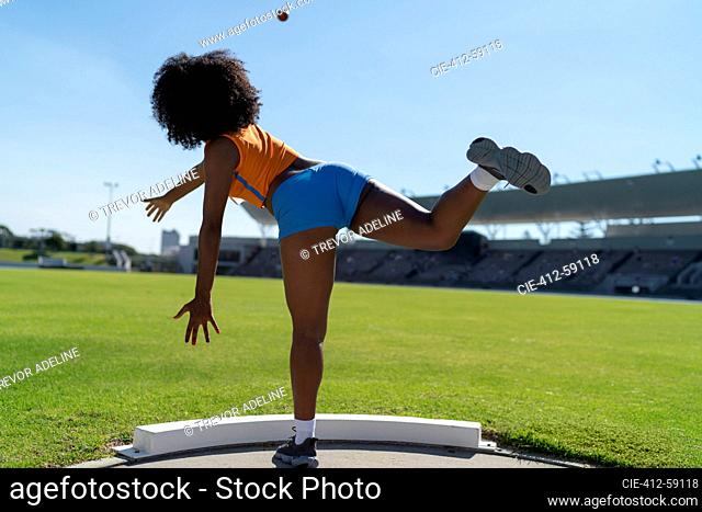 Female track and field athlete throwing shot put in sunny infield