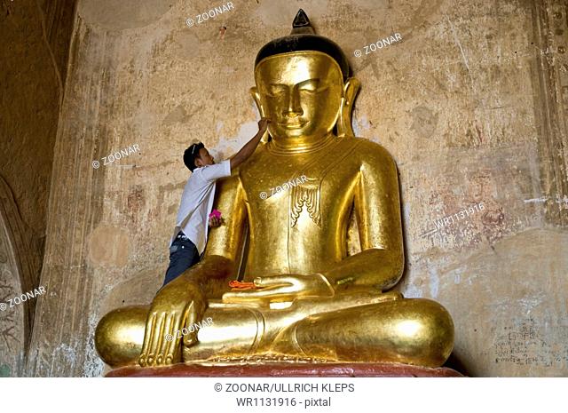 Man applies gold leaf to Buddha image, Burma