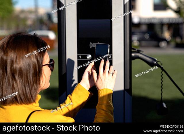 Woman making payment through smart phone at vehicle charging station