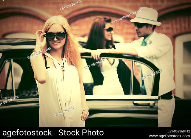 Happy young fashion blond woman in sunglasses next to retro car