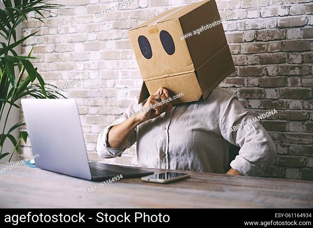 Home worker with paper box on his head. Anonymous people use laptop computer. Concept of doubts and problems with privacy online web protection