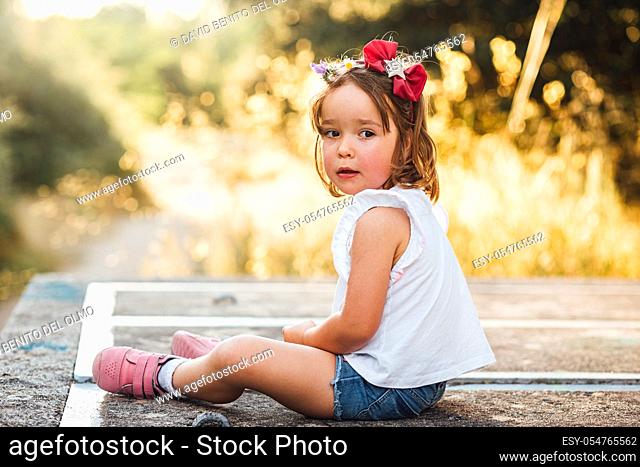 Little blond-haired girl sitting on a concrete platform in the field at sunset