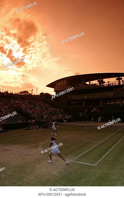 Doubles match on a grass tennis court against a setting sun