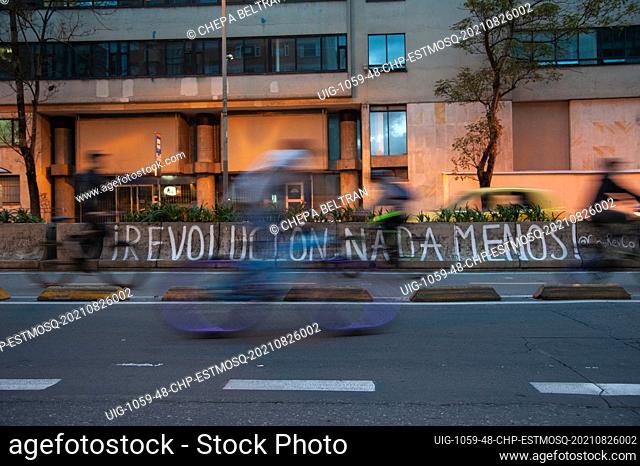 A long exposure shot of a mural that reads ""No Less than Revolution!"" as cyclists pass by during a rally organized by students of the Universidad Distrital
