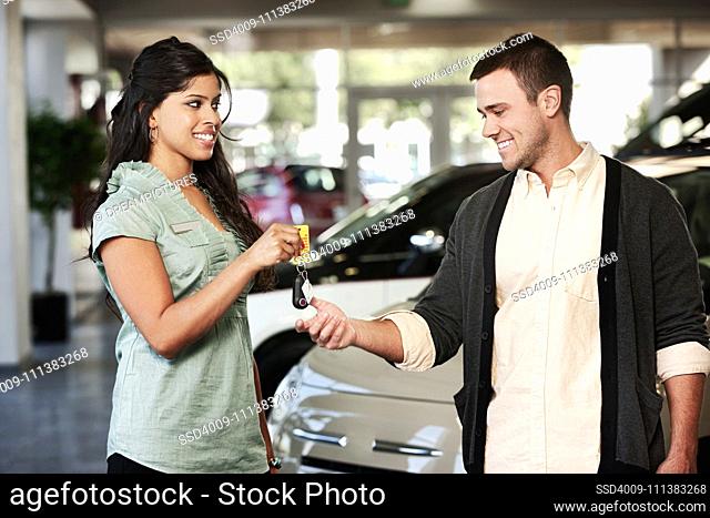 Woman handing man keys to new car in showroom