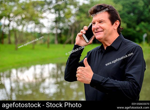 Portrait of mature handsome businessman relaxing at the park outdoors