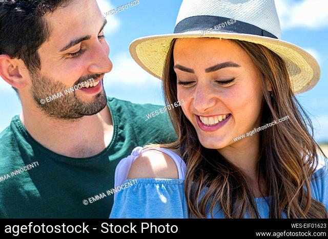 Man looking at smiling girlfriend wearing hat on sunny day