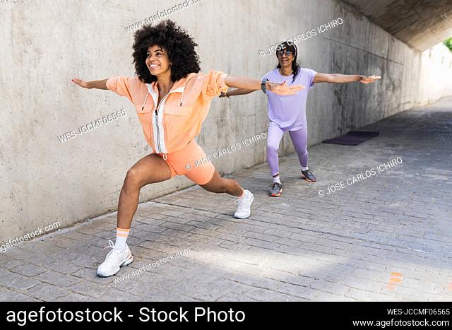 Smiling mother and daughter practicing warrior position on footpath