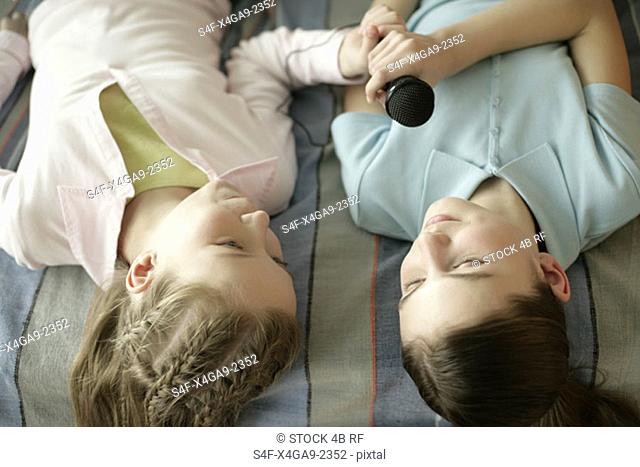 Two friends lying on a bed and holding a microphone