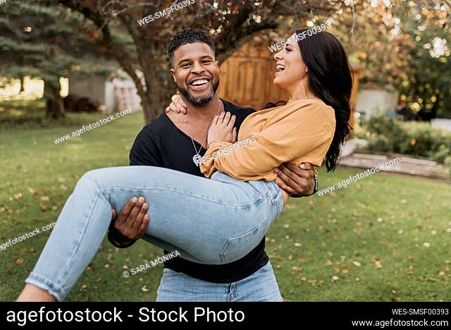 Smiling man carrying woman in arms while standing at backyard