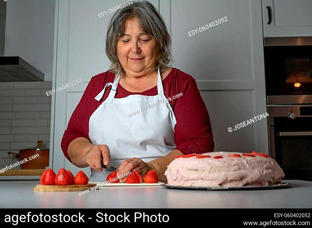 older woman with white hair making a strawberry cake in her home kitchen