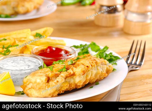 White plate with fish and chips, mayo, ketchup and lemon