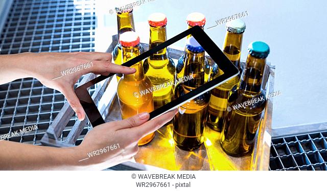 Hands photographing beer bottles through digital tablet at brewery