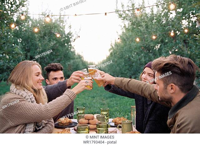An apple orchard in Utah. Group of people toasting with a glass of cider, food and drink on a table