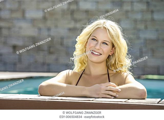 Portrait of a happy blond girl with blue eyes in a pool at the edge