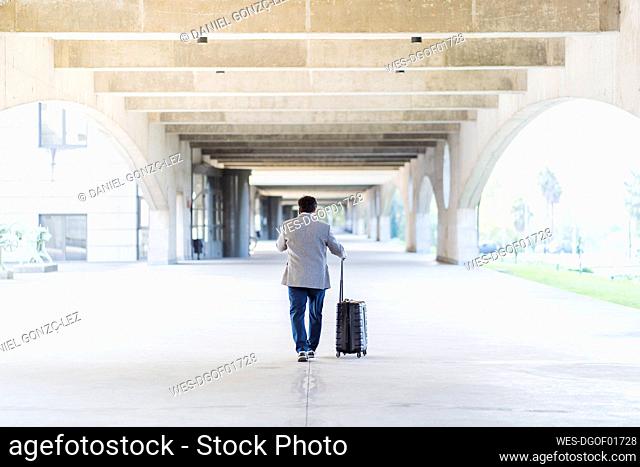Mature businessman with luggage walking in concrete footpath