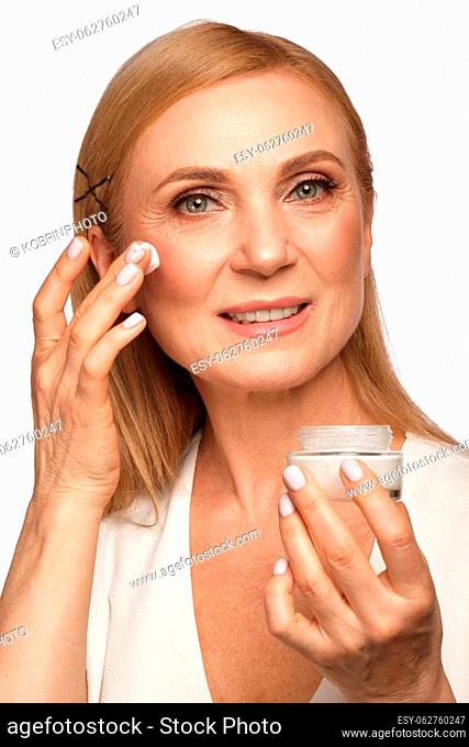 Portrait of a beautiful elderly woman in a white shirt with a moisturizing face cream in her hands