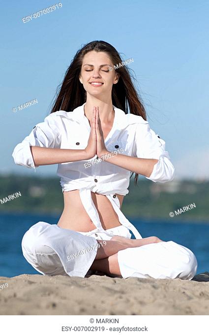 Young beautiful woman practicing yoga on the beach