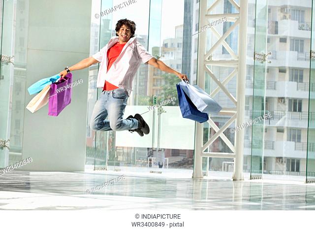 Excited young man jumping with shopping bags