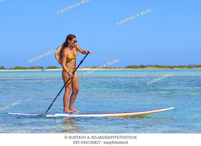 Young Hispanic woman paddling on paddle board or SUP enjoing sport activity in summer time at Caribbean beach with turquoise clear calm waters
