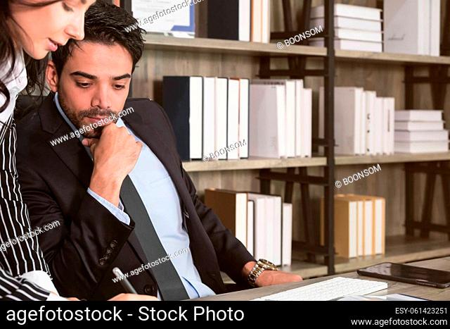 Businessman and businesswoman discussing over documents at desk. Businessman sitting in office desk and looking at paperwork while business woman writing and...