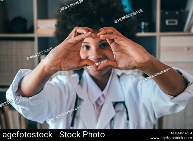 Woman doing heart shape gesture with hands. Smiling black female doctor making a love symbol using her hands. Healthcare worker expressing love and support to...