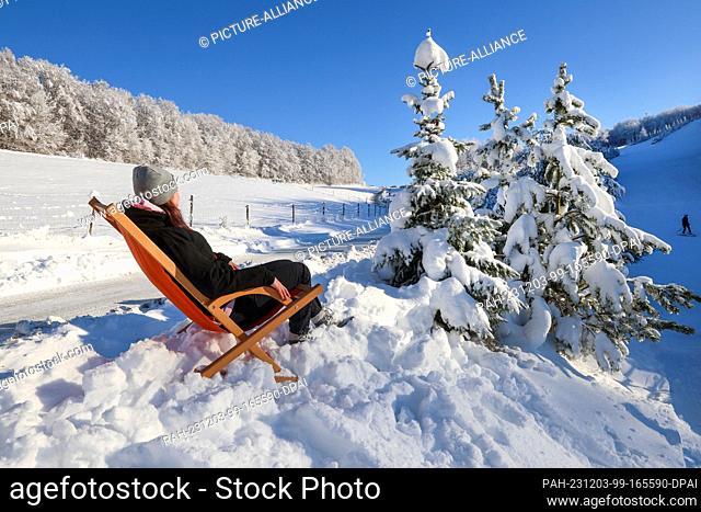 03 December 2023, Baden-Württemberg, Lichtenstein: A woman sunbathes in a deckchair next to a ski resort. After the snow of the last few days
