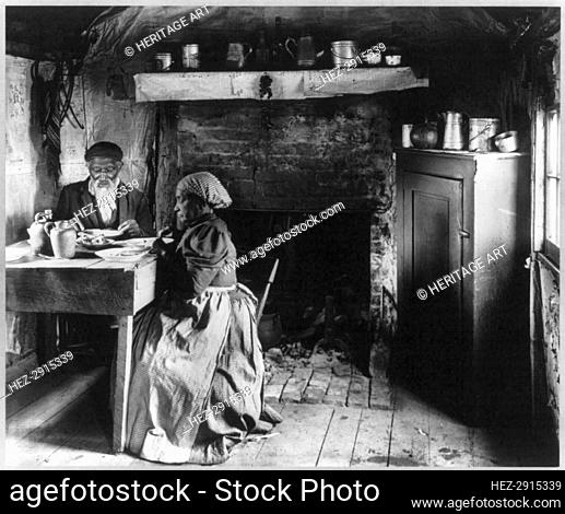 Old African American couple eating at the table by fireplace, rural Virginia, 1899 or 1900. Creator: Frances Benjamin Johnston