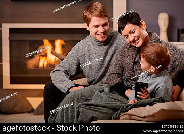 Happy family sitting on couch at home in front of fireplace, smiling