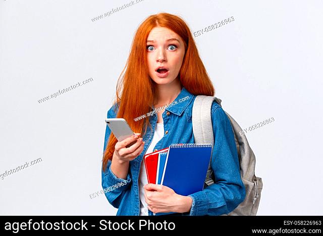 Freshman girl with red long hair, dont know where her class, looking questioned and confused, stare worried, holding smartphone, backpack and notebooks