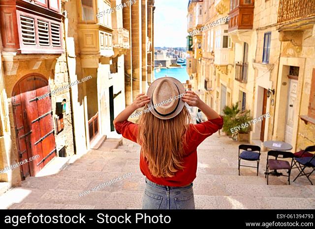 Tourism in Malta. Back view of tourist girl holding hat descends stairs in the old town of Valletta, UNESCO World Heritage, Malta