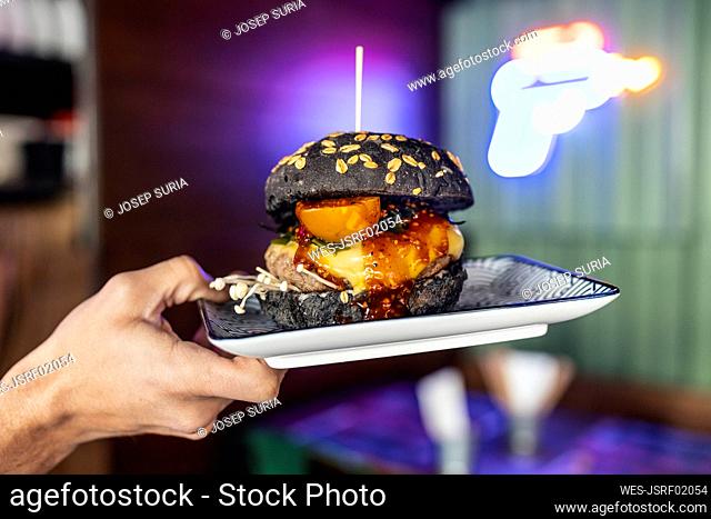 Hands of woman holding black burger on plate at restaurant