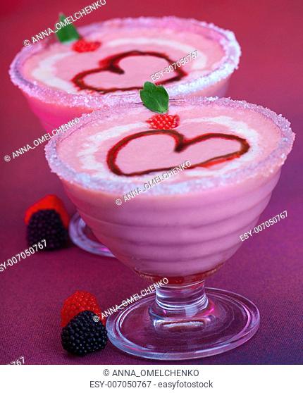 Photo of two glass cups with tasty fruity ice cream isolated on purple background, milk alcoholic beverage with romantic red heart shape, cold creamy cocktail