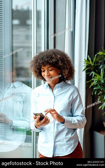 Smiling businesswoman using smart phone by window in office