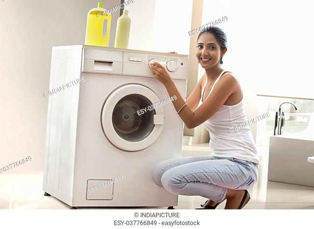 Young woman turning washing machine dial in laundry room