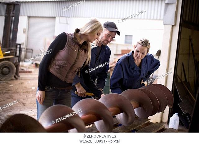 Woman and two workers inspecting machine