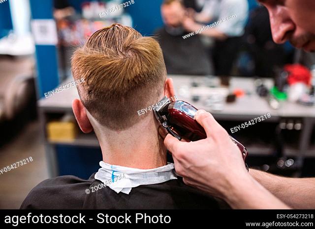 Close up shot of a man getting a trendy haircut at a hair salon. Male caucasian hairdresser serving a client. Man with a beard making haircut with a typewriter...