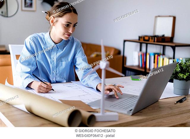 Woman in office working on plan and laptop with wind turbine model on table