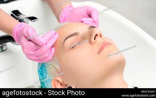 Hairstylist hands in pink gloves washing emerald hair color in professional beauty salon. Head of young woman with closed eyes in special sink hair salon
