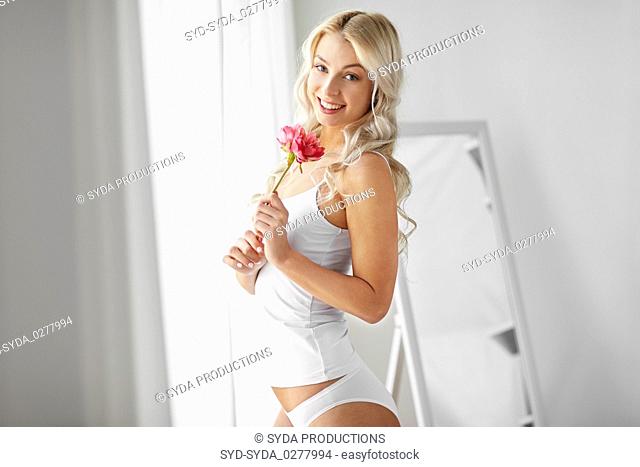 woman in underwear smelling flower at window