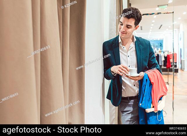 Man in fashion store waiting for his woman to appear from the fitting room being a bit bored