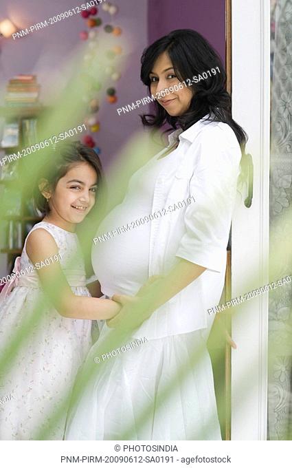 Girl and her pregnant mother standing together and smiling
