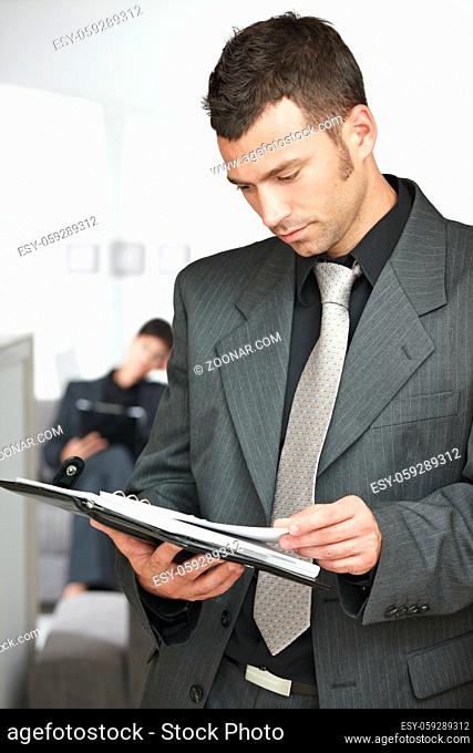Young businessman standing in doorway at office, looking at organizer