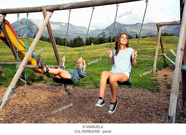 Two female adult friends playing on swings in Austrian Alps, Sattelbergalm, Tirol, Austria