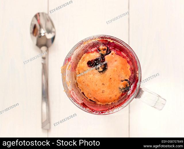 Mug Cake in glass mug with berries on white wooden background. Top view or flat lay