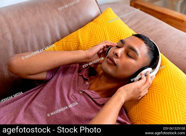 Mixed race man lying on couch wearing headphones and listening to music